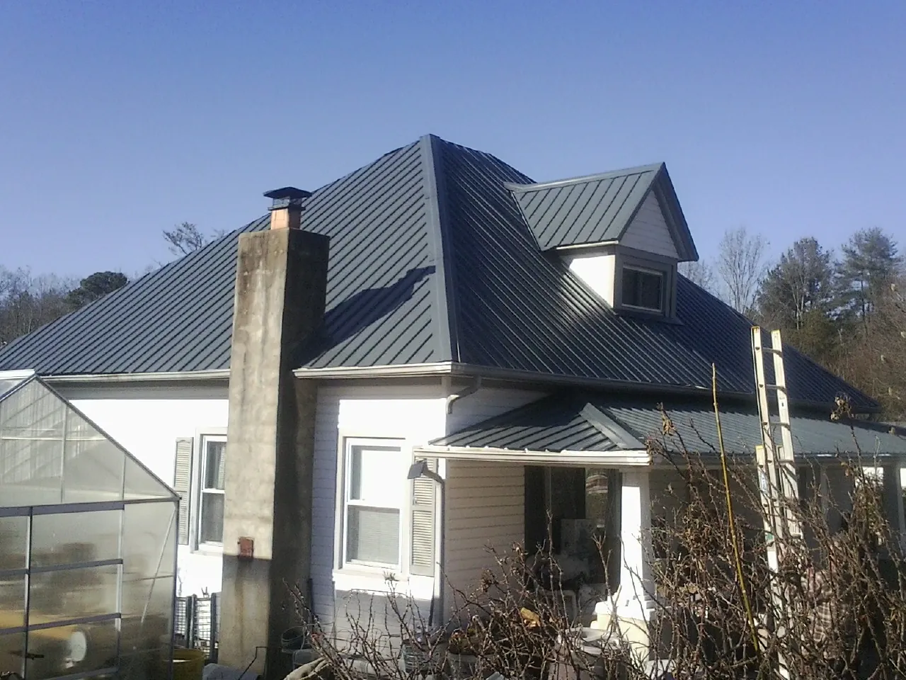 Dark blue standing seam metal roof on a white farmhouse with dormer — Slate & Tile Roof Repair by Roofing Brothers in Ortonville