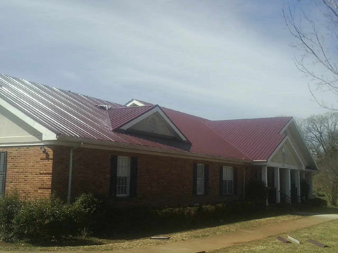 Red metal roof with gabled entries on a long brick building, from a Hail Damage Roof Repair job in Ortonville