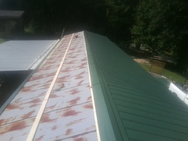 Old rusted panels beside newly installed green metal roofing — Wind Damage Roof Repair by Roofing Brothers in Ortonville