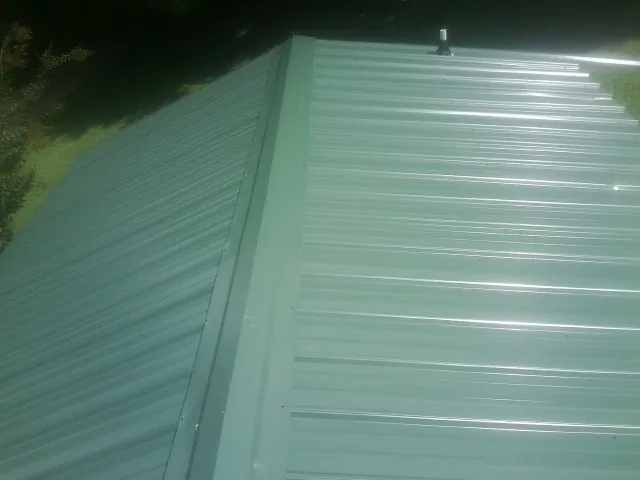 New green metal panels meeting at the ridge of a roof — Flat Roof Repair work by our crew in Ortonville