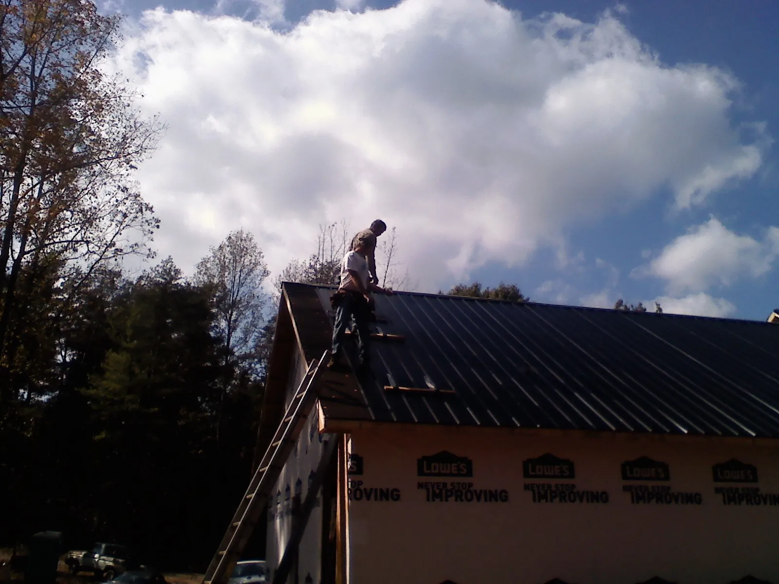 Roofer fastening dark metal panels high against a cloudy sky, from a Roof Inspection job in Ortonville