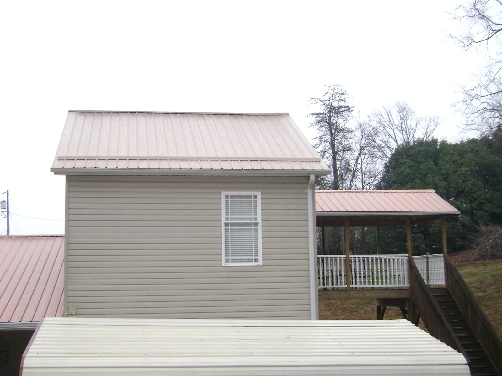 Tan metal roofs on a two story addition and attached porch, from a Roof Replacement job in Ortonville